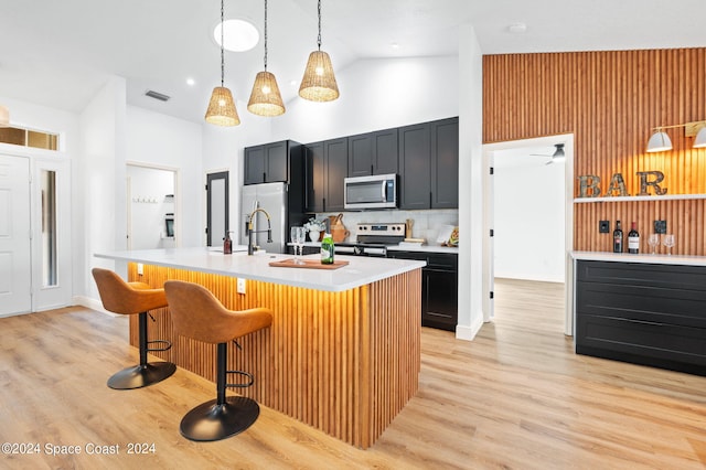 kitchen with a breakfast bar, a kitchen island with sink, hanging light fixtures, stainless steel appliances, and light hardwood / wood-style floors