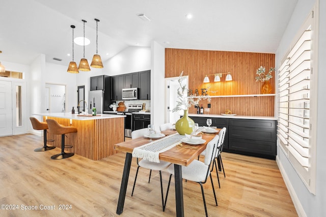 dining space featuring high vaulted ceiling, wooden walls, and light wood-type flooring