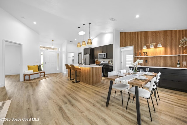 dining area with high vaulted ceiling, wooden walls, and light hardwood / wood-style floors