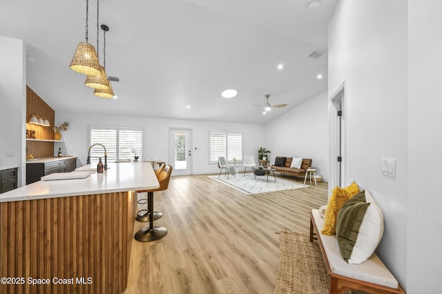 kitchen featuring lofted ceiling, hanging light fixtures, light wood-type flooring, an island with sink, and ceiling fan