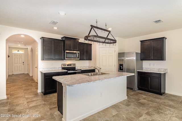 kitchen featuring appliances with stainless steel finishes, a textured ceiling, dark brown cabinets, a kitchen island with sink, and sink