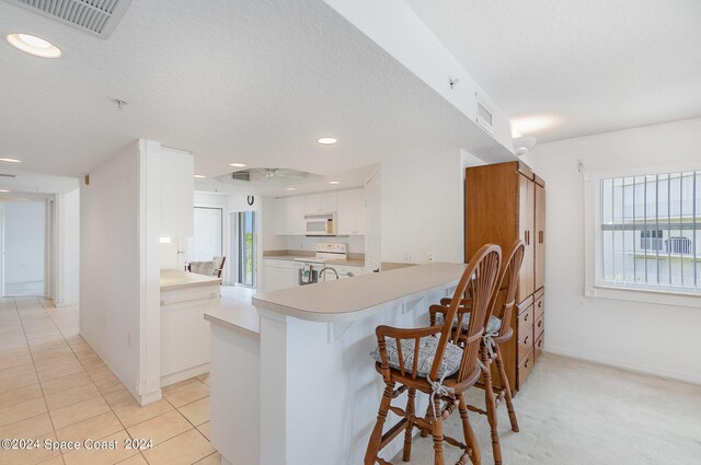 kitchen with ceiling fan, kitchen peninsula, white appliances, white cabinetry, and a breakfast bar area