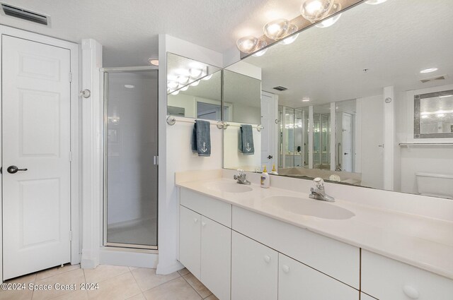 bathroom featuring a textured ceiling, a shower with door, tile patterned floors, vanity, and toilet