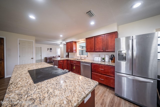 kitchen featuring light wood-type flooring, light stone counters, a center island, stainless steel appliances, and ceiling fan