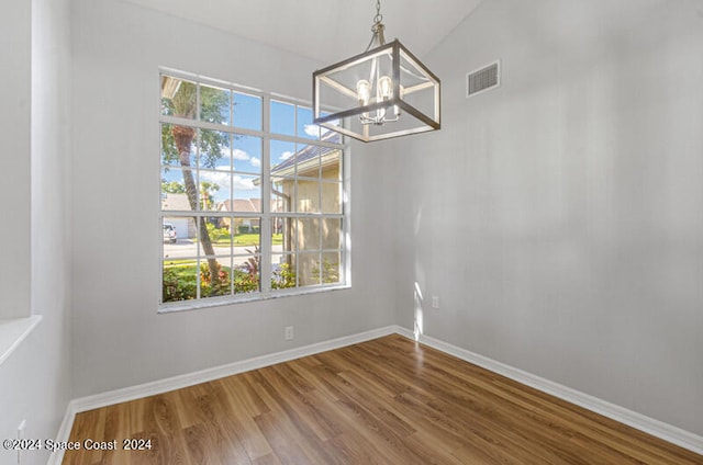 unfurnished dining area with wood-type flooring, vaulted ceiling, an inviting chandelier, and a wealth of natural light