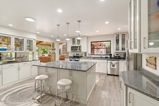 kitchen with decorative light fixtures, appliances with stainless steel finishes, a center island, a breakfast bar area, and light hardwood / wood-style floors