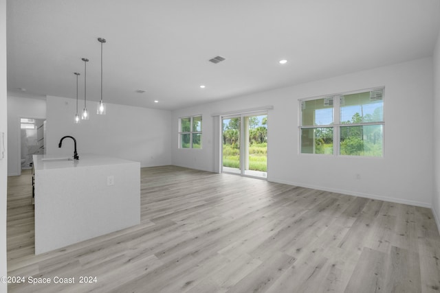unfurnished living room featuring light wood finished floors, a sink, visible vents, baseboards, and recessed lighting