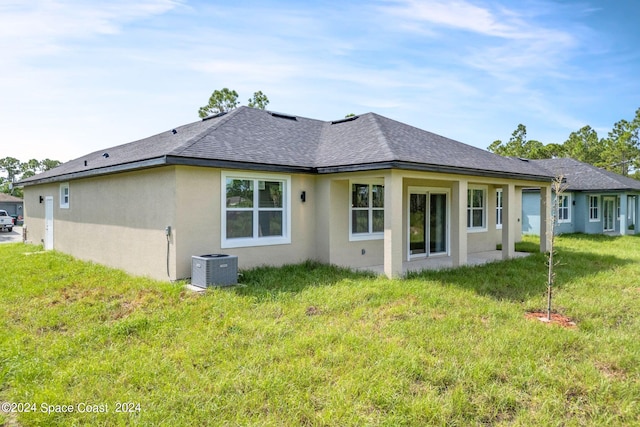 rear view of house with stucco siding, roof with shingles, central AC unit, and a lawn