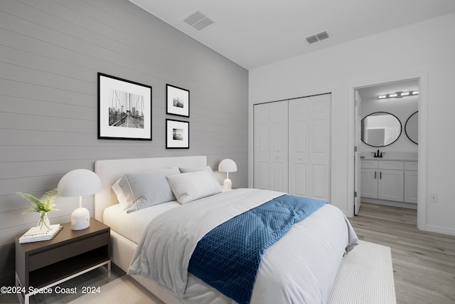 bedroom with light wood-style floors, connected bathroom, visible vents, and a sink