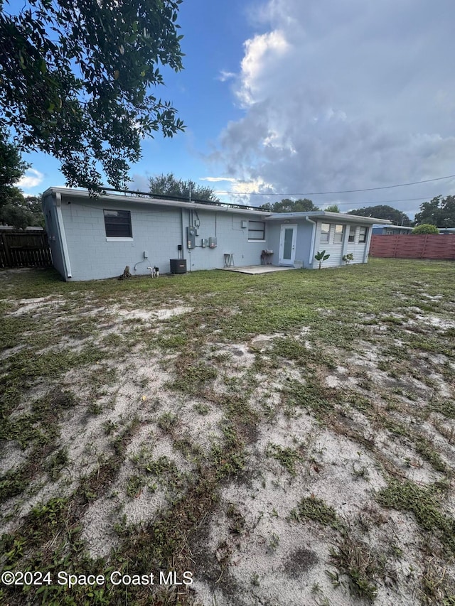 rear view of house featuring central AC unit and a lawn