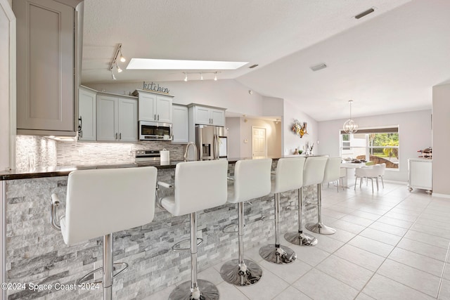 kitchen with light tile patterned floors, gray cabinets, stainless steel appliances, lofted ceiling with skylight, and decorative backsplash