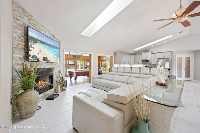 tiled living room with ceiling fan, vaulted ceiling with skylight, and a fireplace