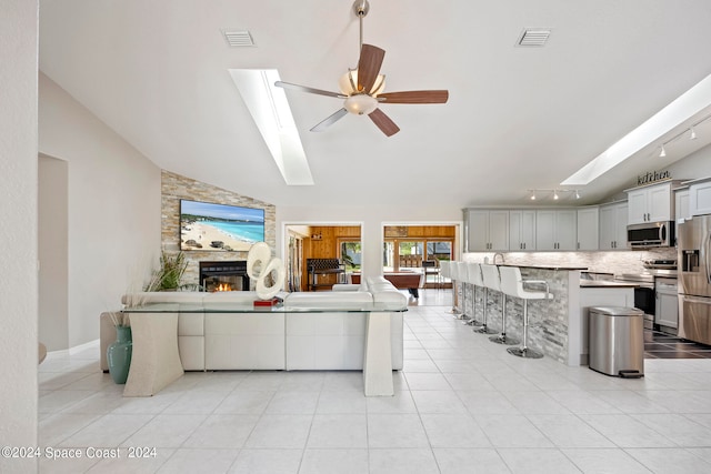 living room featuring vaulted ceiling with skylight, a fireplace, light tile patterned floors, and ceiling fan