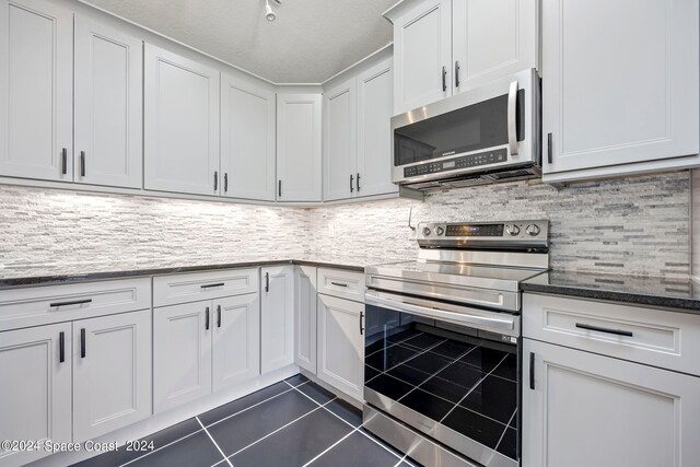 kitchen with dark tile patterned flooring, white cabinetry, stainless steel appliances, dark stone countertops, and decorative backsplash