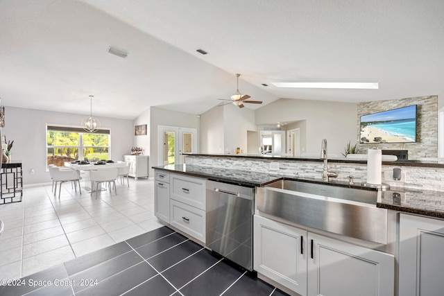 kitchen featuring dishwasher, white cabinets, lofted ceiling with skylight, dark stone countertops, and ceiling fan