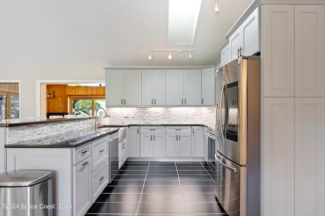 kitchen featuring appliances with stainless steel finishes, white cabinetry, a skylight, dark stone counters, and sink