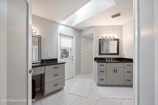 bathroom with vanity, a skylight, a shower, and tile patterned floors