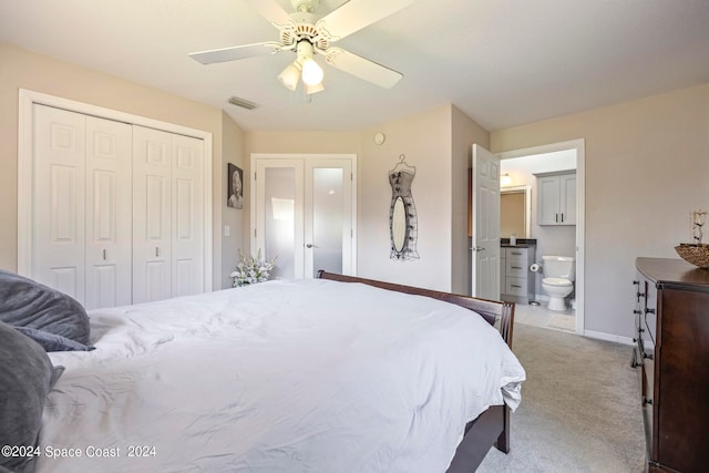 bedroom with a closet, ensuite bath, ceiling fan, and light colored carpet