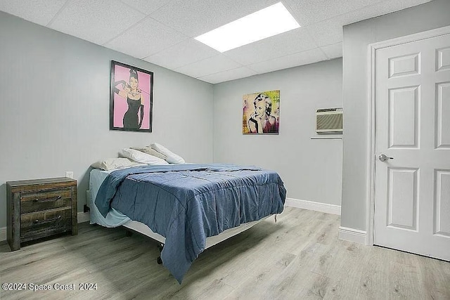 bedroom with a paneled ceiling, light hardwood / wood-style flooring, and a wall unit AC