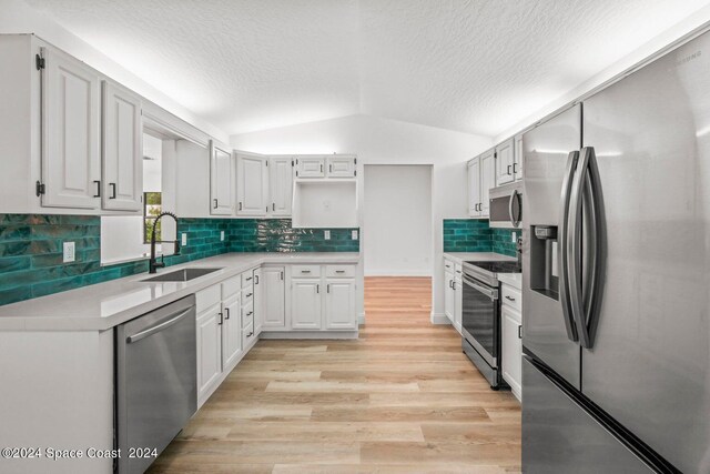 kitchen featuring appliances with stainless steel finishes, vaulted ceiling, white cabinets, light hardwood / wood-style flooring, and sink