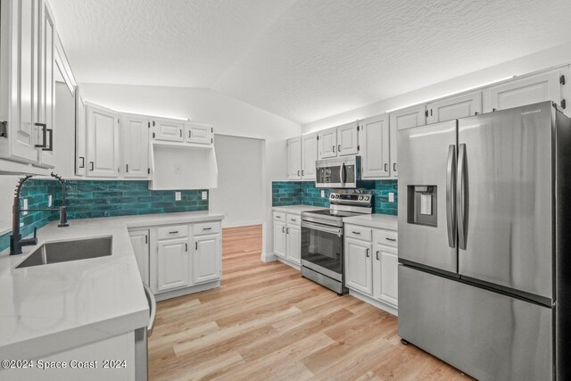 kitchen with lofted ceiling, stainless steel appliances, and white cabinets