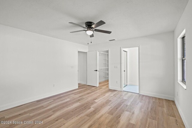 unfurnished bedroom with ceiling fan, light hardwood / wood-style flooring, a closet, and a spacious closet