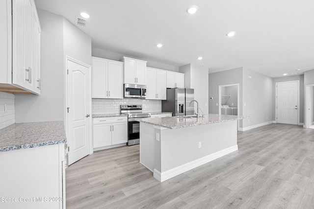 kitchen with light stone counters, washer and dryer, white cabinetry, stainless steel appliances, and a center island with sink