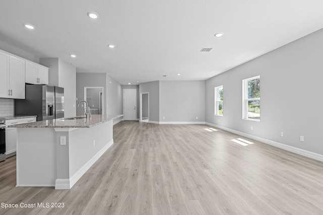 kitchen with sink, an island with sink, white cabinets, light hardwood / wood-style flooring, and stainless steel appliances