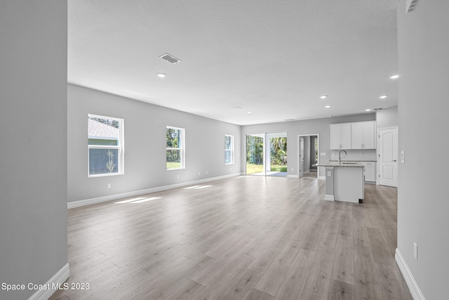 unfurnished living room featuring a textured ceiling, light wood-type flooring, and sink