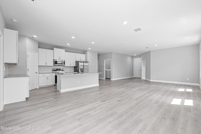 kitchen with light wood-type flooring, an island with sink, white cabinetry, backsplash, and appliances with stainless steel finishes