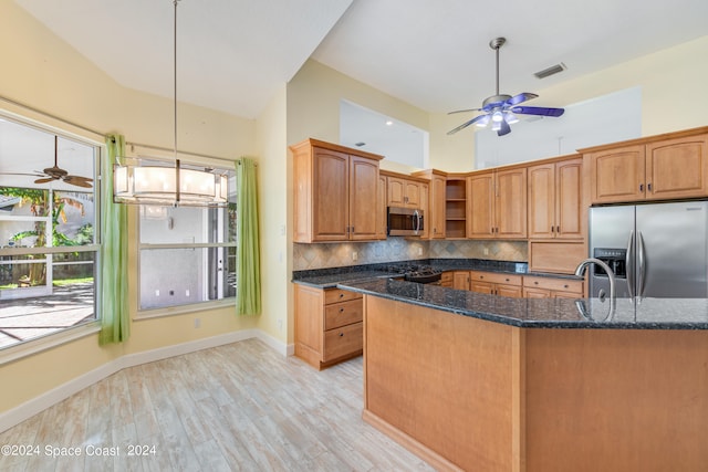 kitchen featuring tasteful backsplash, light hardwood / wood-style flooring, dark stone countertops, decorative light fixtures, and appliances with stainless steel finishes