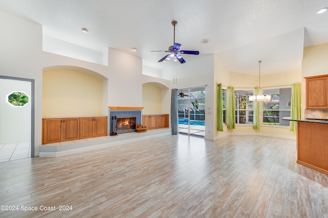 unfurnished living room featuring ceiling fan, a high ceiling, a fireplace, light hardwood / wood-style flooring, and a textured ceiling