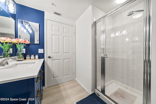 bathroom with wood-type flooring, a textured ceiling, walk in shower, and vanity