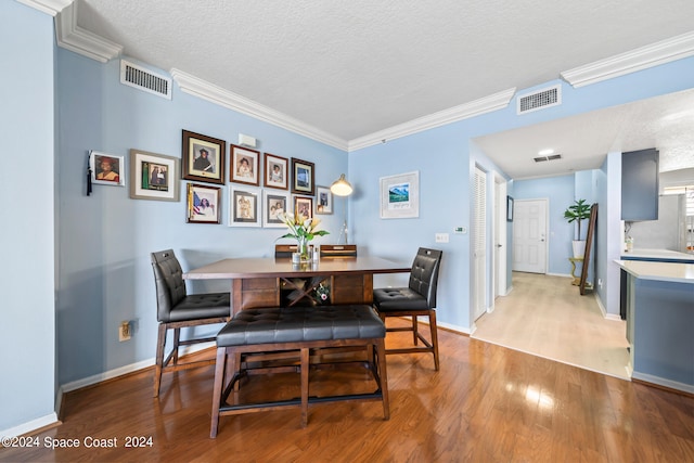 dining room featuring a textured ceiling, light hardwood / wood-style flooring, and crown molding