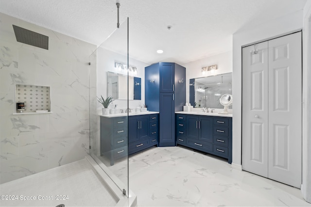 bathroom with a textured ceiling, tiled shower, and vanity