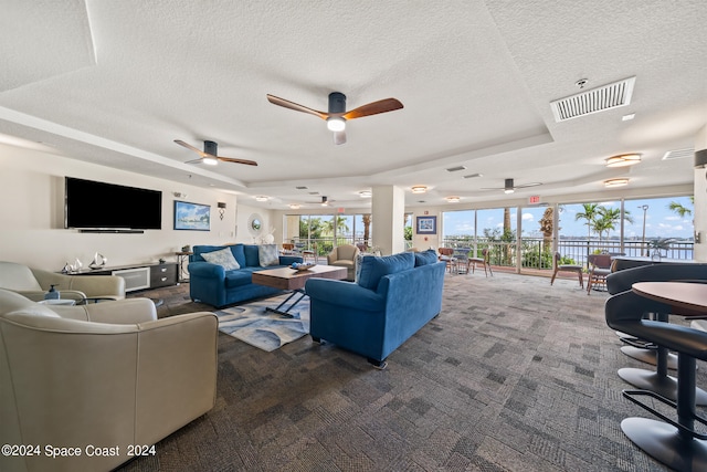 living room with ceiling fan, a textured ceiling, a raised ceiling, and dark colored carpet