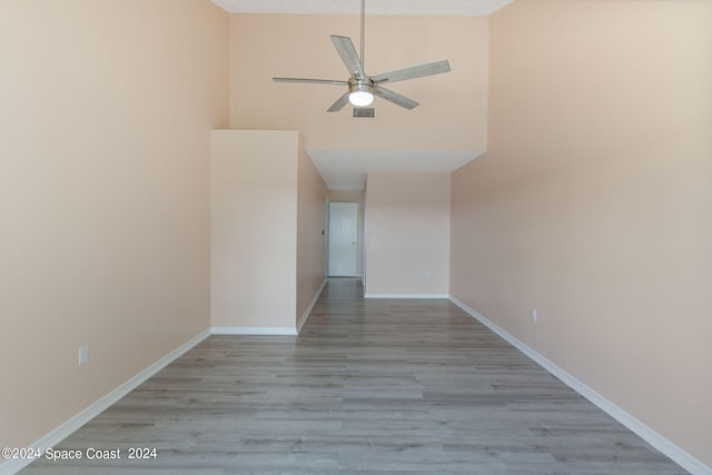 empty room with ceiling fan, a towering ceiling, and light wood-type flooring