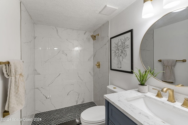 bathroom featuring a tile shower, vanity, a textured ceiling, and toilet