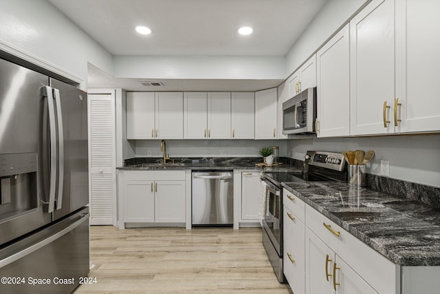 kitchen featuring white cabinets, sink, light hardwood / wood-style flooring, dark stone countertops, and appliances with stainless steel finishes