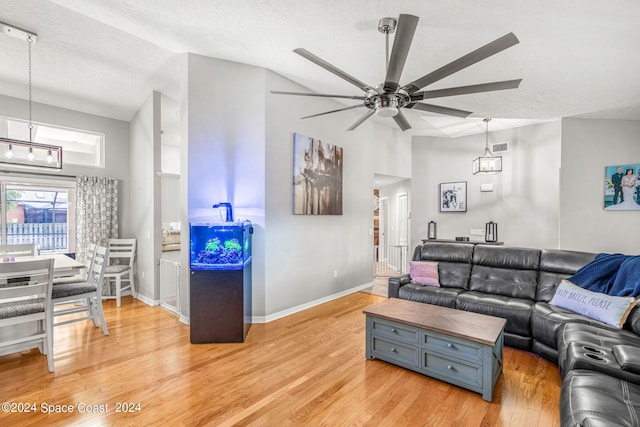 living room featuring light wood-type flooring, vaulted ceiling, ceiling fan, and a textured ceiling