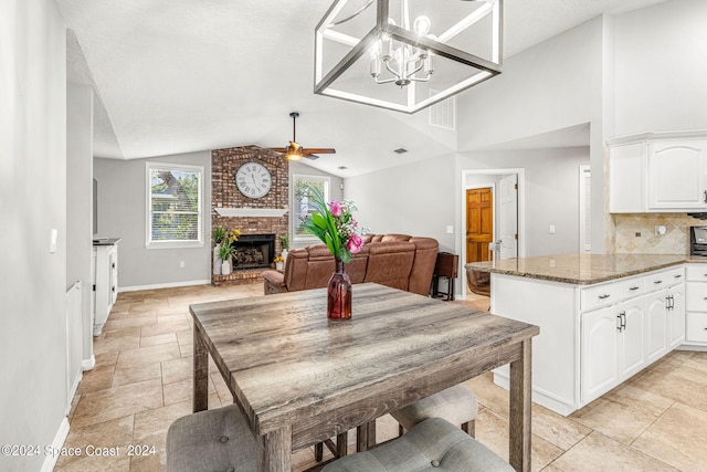 dining room featuring ceiling fan with notable chandelier, a brick fireplace, vaulted ceiling, and a textured ceiling