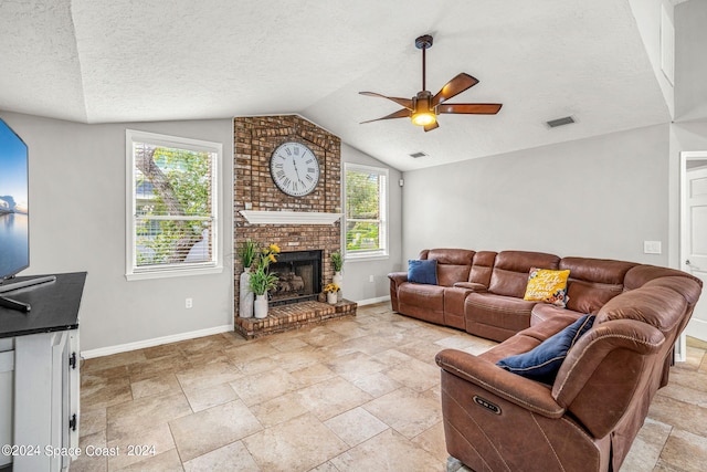 living room featuring a textured ceiling, lofted ceiling, ceiling fan, and a brick fireplace