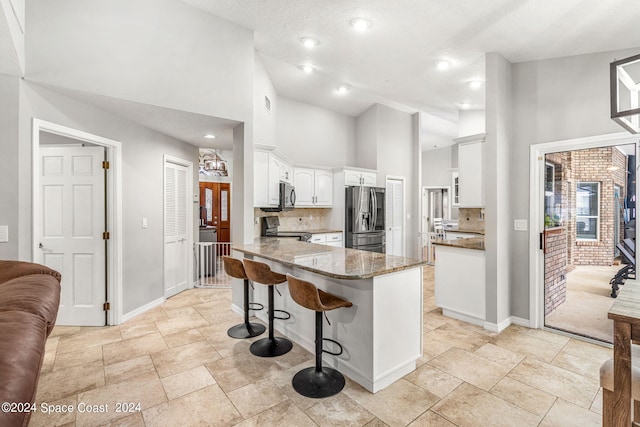 kitchen with white cabinets, kitchen peninsula, appliances with stainless steel finishes, dark stone countertops, and a towering ceiling