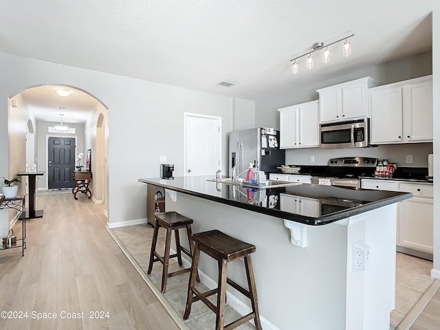 kitchen with a breakfast bar, light hardwood / wood-style floors, white cabinetry, stainless steel appliances, and a center island with sink