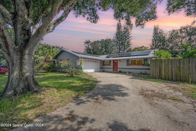 ranch-style home with a garage, solar panels, and a yard