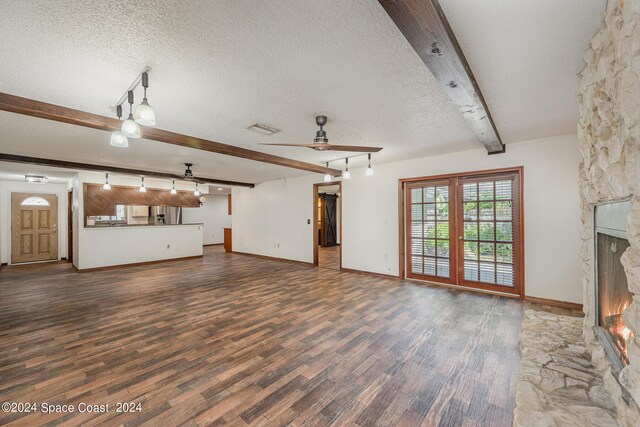 unfurnished living room featuring dark wood-type flooring, a fireplace, beamed ceiling, a textured ceiling, and ceiling fan