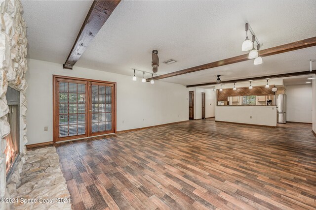 unfurnished living room featuring a stone fireplace, hardwood / wood-style flooring, beam ceiling, and a textured ceiling