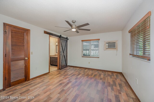 unfurnished bedroom featuring ceiling fan, multiple windows, hardwood / wood-style floors, and a barn door