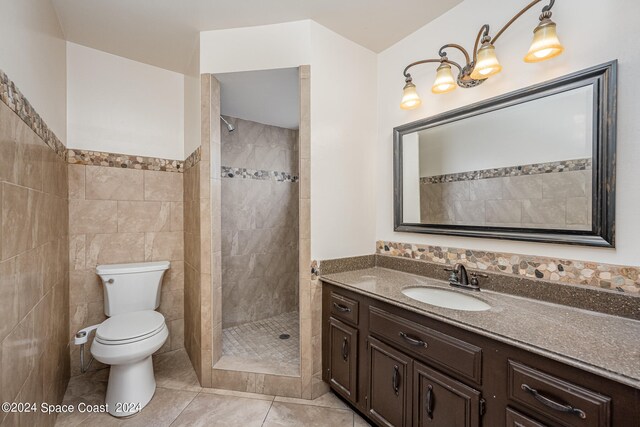 bathroom featuring a tile shower, tile walls, tile patterned flooring, vanity, and toilet