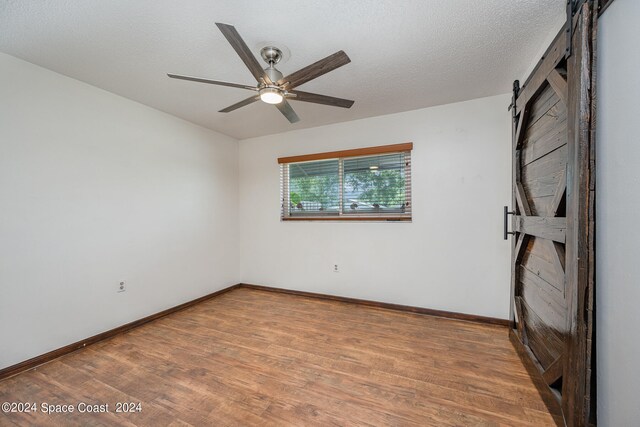 unfurnished room featuring ceiling fan, hardwood / wood-style flooring, a barn door, and a textured ceiling